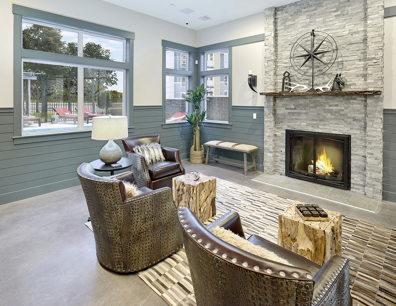 The clubhouse at Woodcreek Apartments with a fireplace, may windows, chairs and tables.